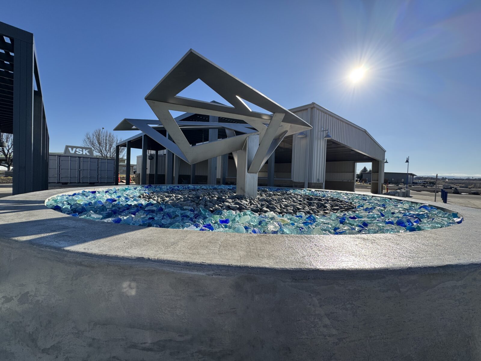 A progress photo showing the renovation of two former hangar buildings into open-air pavilions and a new stylized “paper airplane” art installation at Vista Field.